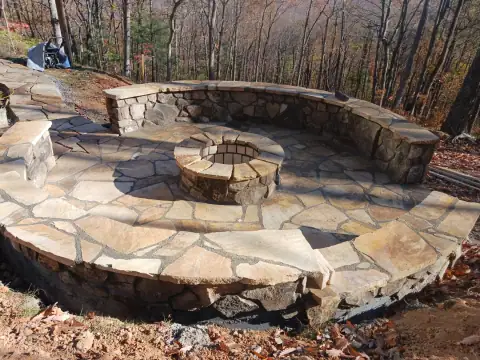 Raised flagstone patio with a round fire pit and stone seating by F. Stone Designs