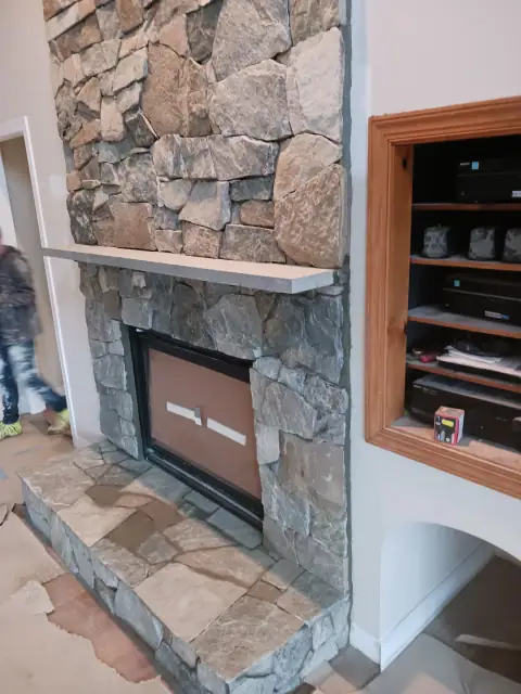 Completed stone fireplace with wood mantel and built-in cabinetry