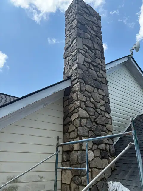 Stone chimney construction with scaffolding beside the house